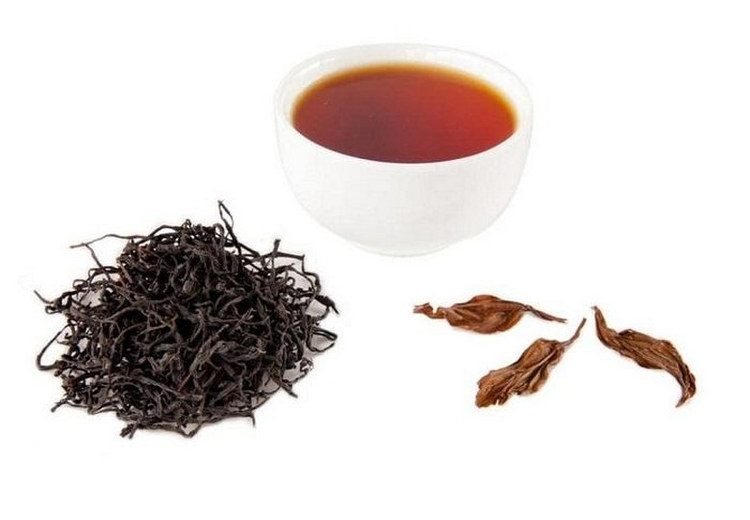 Chén trà đen màu đỏ hổ phách bên cạnh lá trà khô