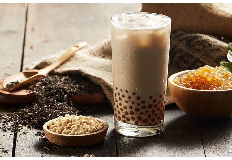 Ly trà sữa trân châu bên cạnh lá trà khô và bát trân châu